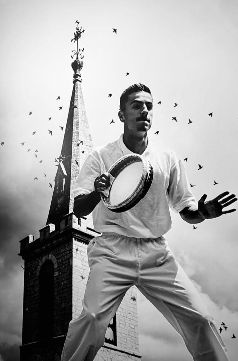 Photographie ancienne en noir et blanc : un joueur de balle au tambourin en pleine frappe devant un clocher